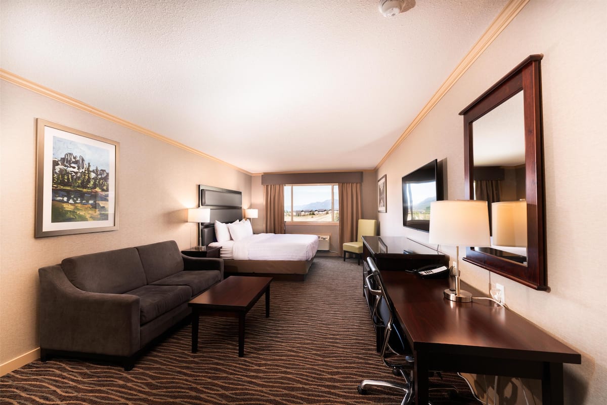 A hotel room with a bed, a sofa, a desk, a TV, and a large mirror.