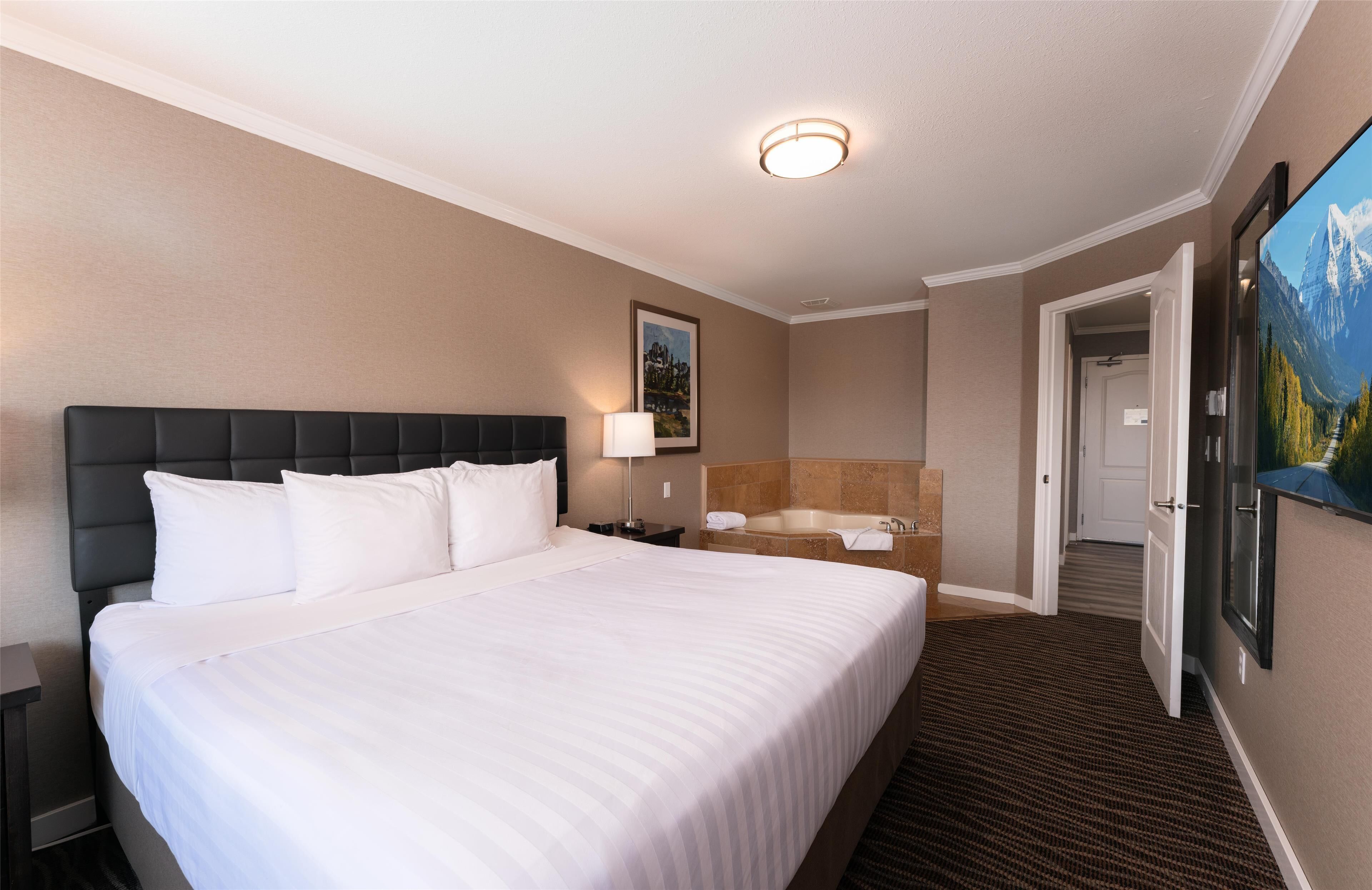 A hotel room with a large bed, a bathroom with a bathtub, and a painting on the wall.