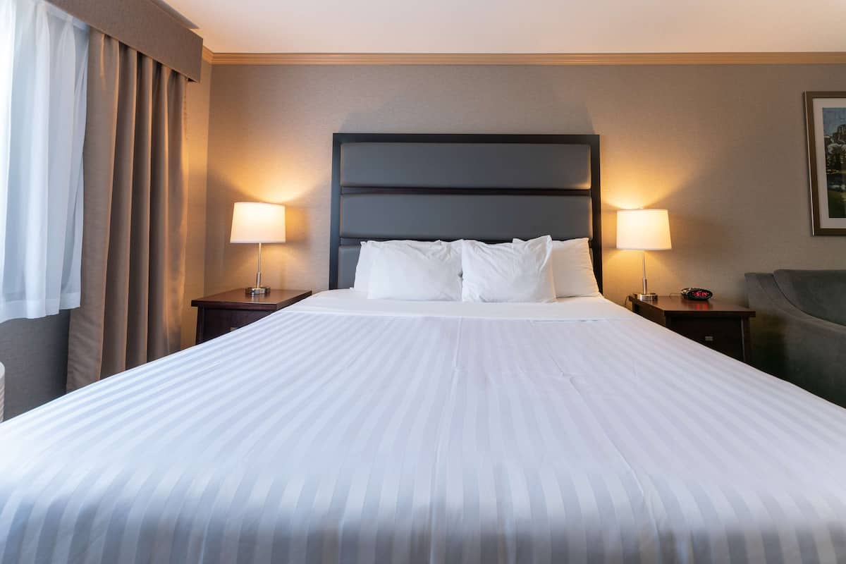 A hotel room with a large bed, two bedside tables with lamps, a headboard, and a framed picture on the wall.