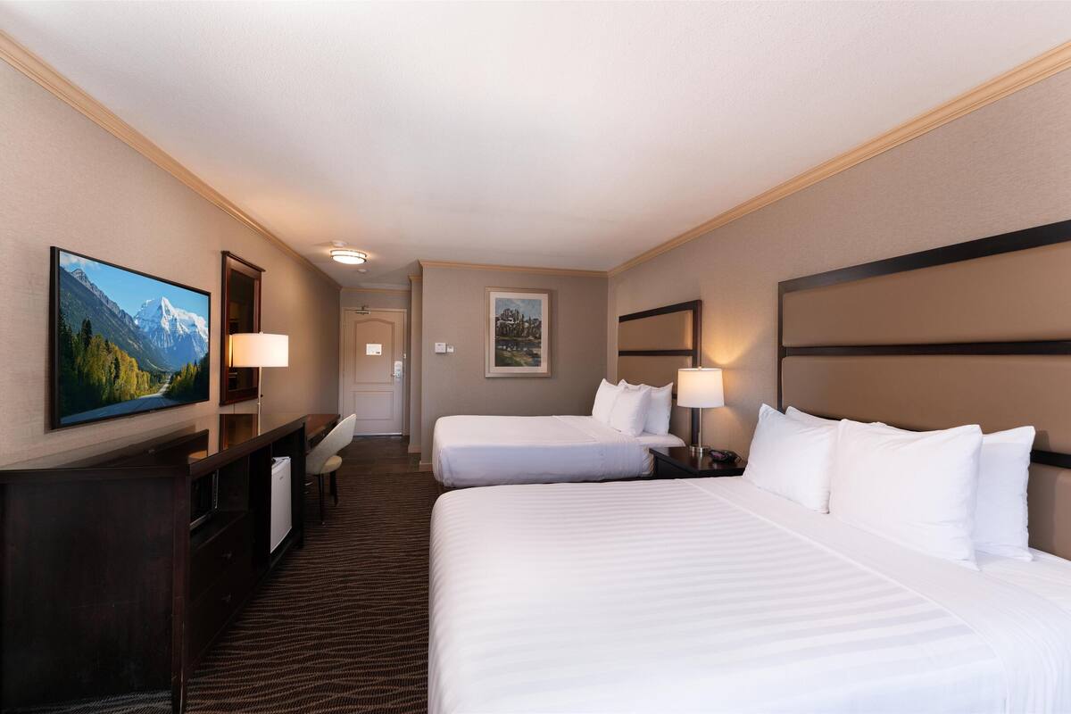 A hotel room with two beds, a desk, a TV, and a framed picture on the wall.