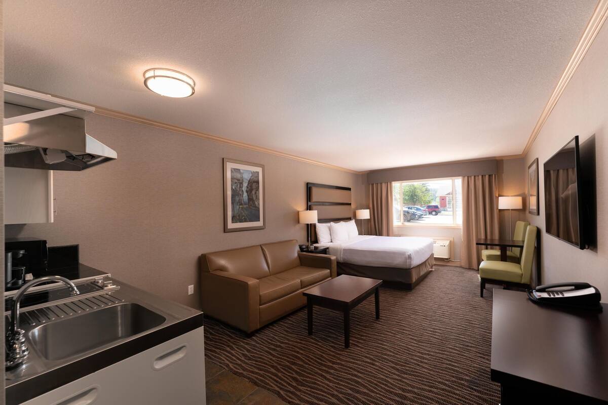A hotel room with a kitchenette, a bed, a sofa, a desk, and a chair.
