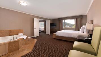 A hotel room with a large bed, a separate bathroom with a bathtub, a flat-screen TV, and a view of the outdoors.