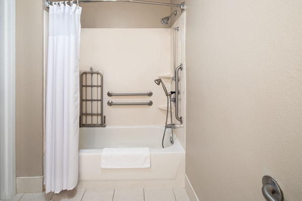 A bathroom with a bathtub, grab bars, a showerhead, and a towel rack.