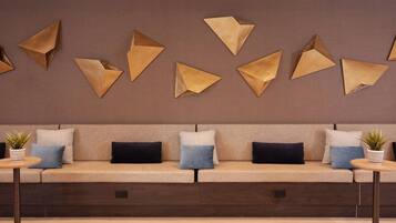 A modern lounge area with a sofa, decorative wall art, and small tables with potted plants.