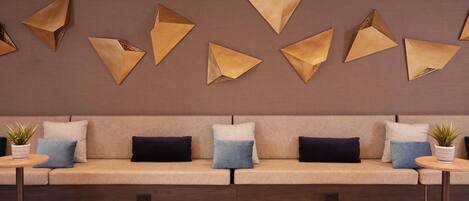 A modern lounge area with a sofa, decorative wall art, and small tables with potted plants.