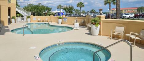 A hotel pool area with two pools, lounge chairs, and a palm tree.