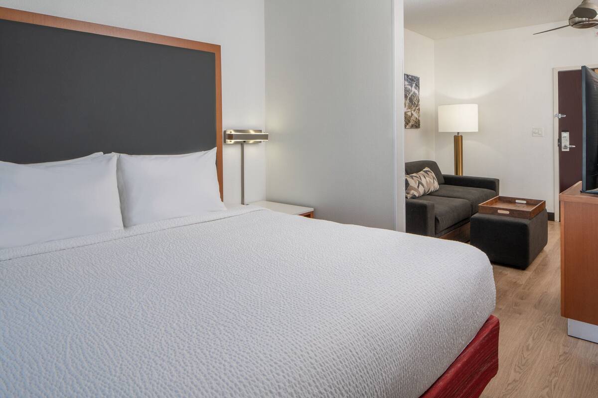 A hotel room with a large bed, a desk, a chair, a sofa, and a lamp.