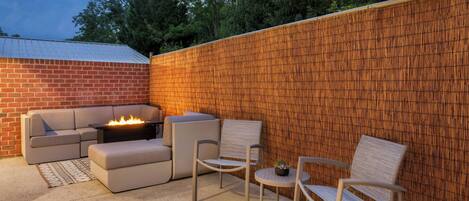 Un patio con pared de ladrillo, un brasero, un sofá y dos sillones.