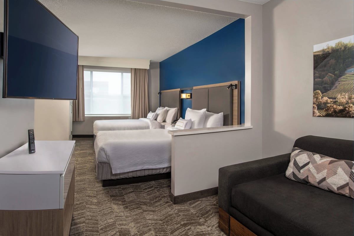 A hotel room with two beds, a desk, a TV, and a couch.