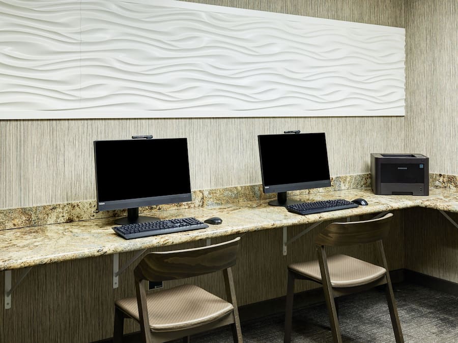 Um espaço de trabalho moderno com dois monitores de computador, teclado e computador de mesa Samsung. Há duas cadeiras bege e uma bancada de mármore.