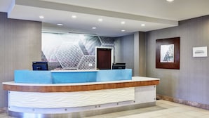 Una recepción de hotel con diseño moderno, una pantalla digital y un letrero con el nombre del hotel.