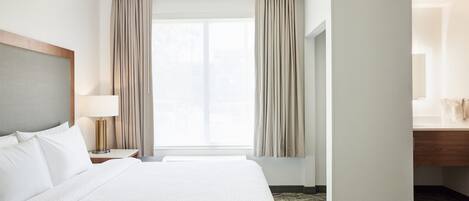A hotel room with a large bed, a nightstand with a lamp, a window with curtains, and a wooden headboard.