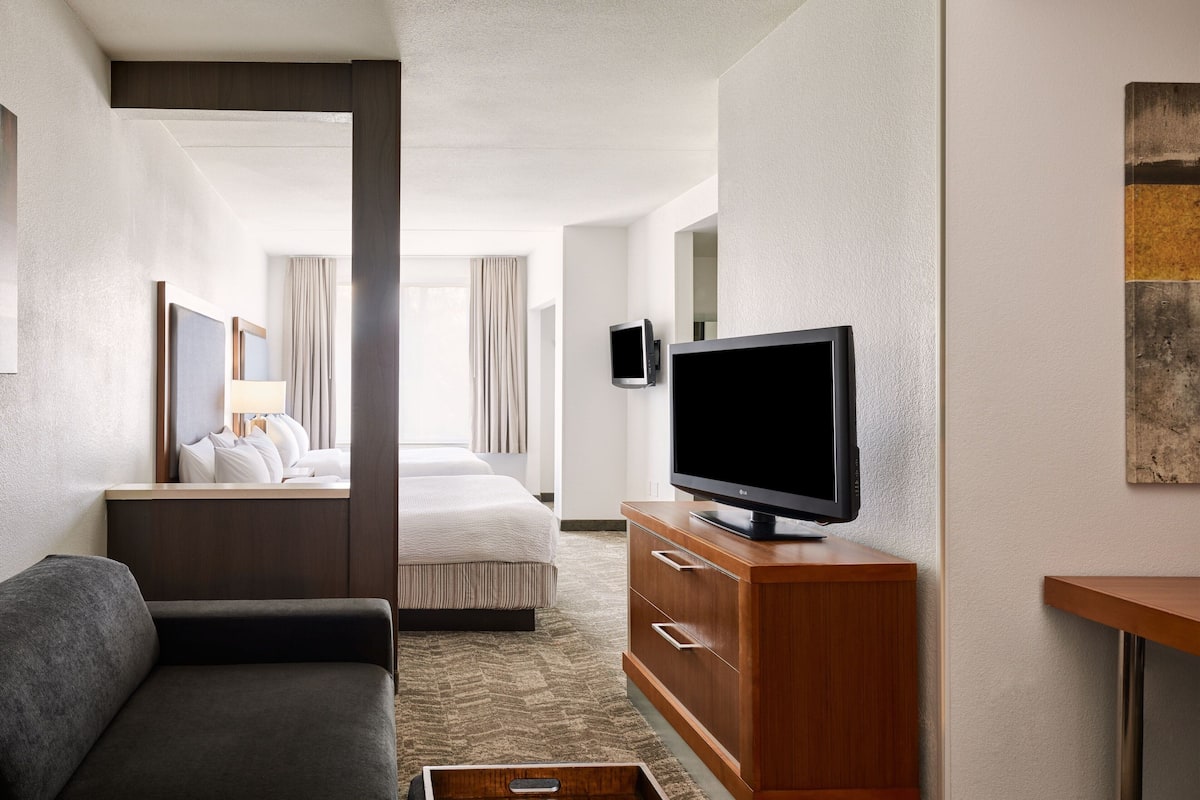 A hotel room with a bed, a TV on a wooden cabinet, a sofa, and a small table.