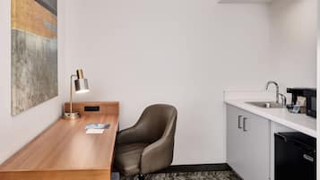 Una cocina compacta con un escritorio de madera, una silla, una lámpara moderna, un lavamanos y una cafetera.