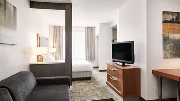 Una habitación de hotel moderna con sofá, televisión sobre un mueble de madera, cama con cortinas y un ventanal grande.