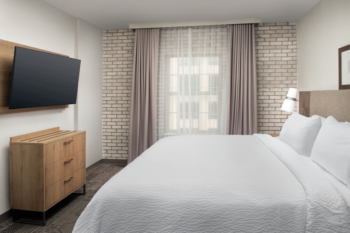 Une chambre d’hôtel avec un lit, un téléviseur fixé au mur, une commode en bois et un mur en briques.