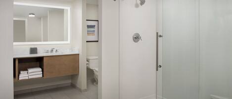 A modern bathroom with a glass-enclosed shower, a white sink with a wooden vanity, and a framed picture on the wall.