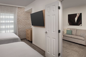 Ein Hotelzimmer mit zwei Betten, einem an der Wand montierten Fernseher, einem Sofa und einer Ziegelwand.
