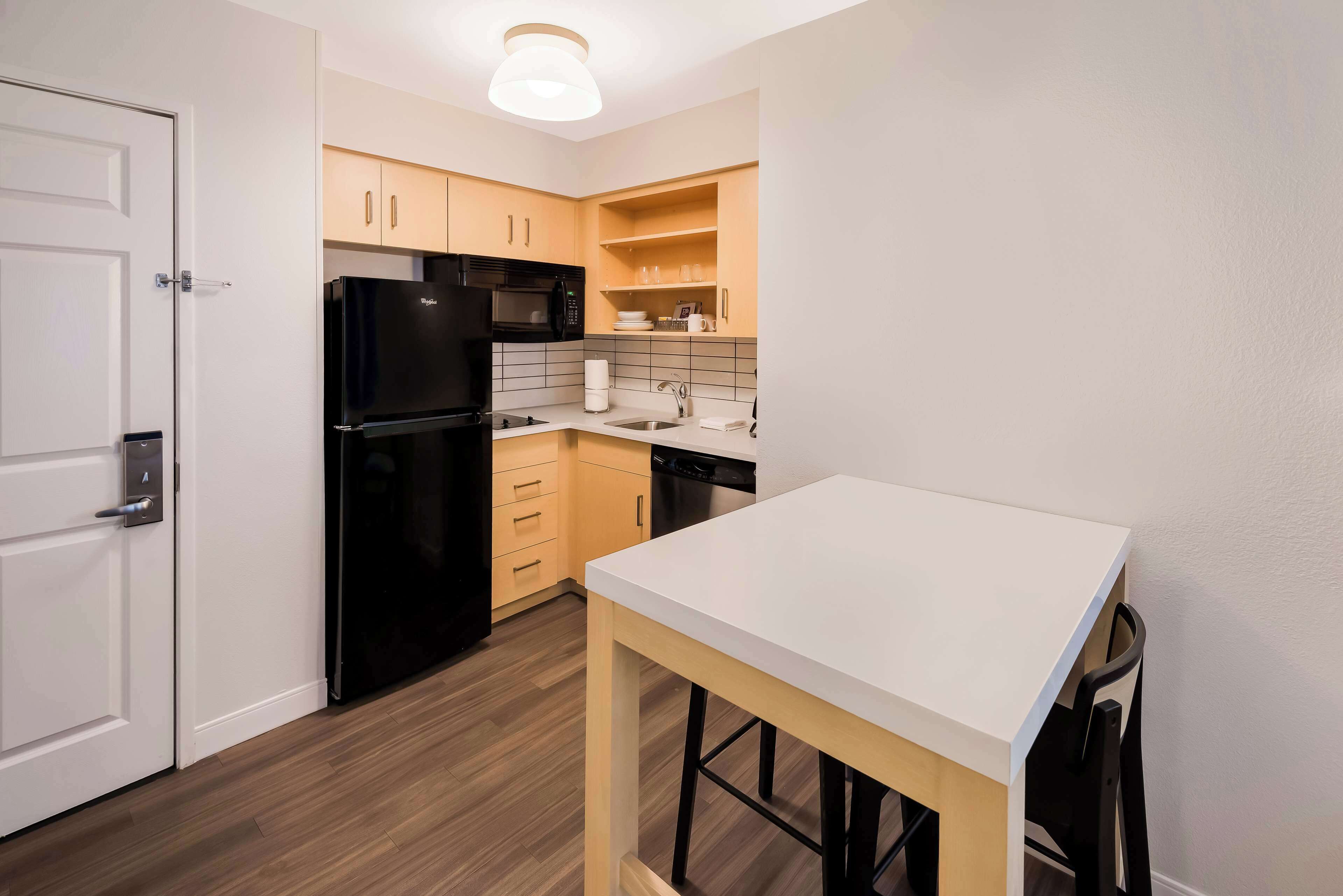 Cocina compacta con refrigerador, microondas, lavamanos y armarios de madera.