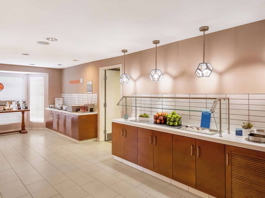 A modern kitchen with wooden cabinets, a countertop with various food items, and pendant lights.