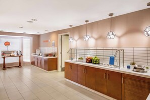 A modern kitchen with wooden cabinets, a countertop with various food items, and pendant lights. - Sonesta ES Suites Andover Boston (Andover)