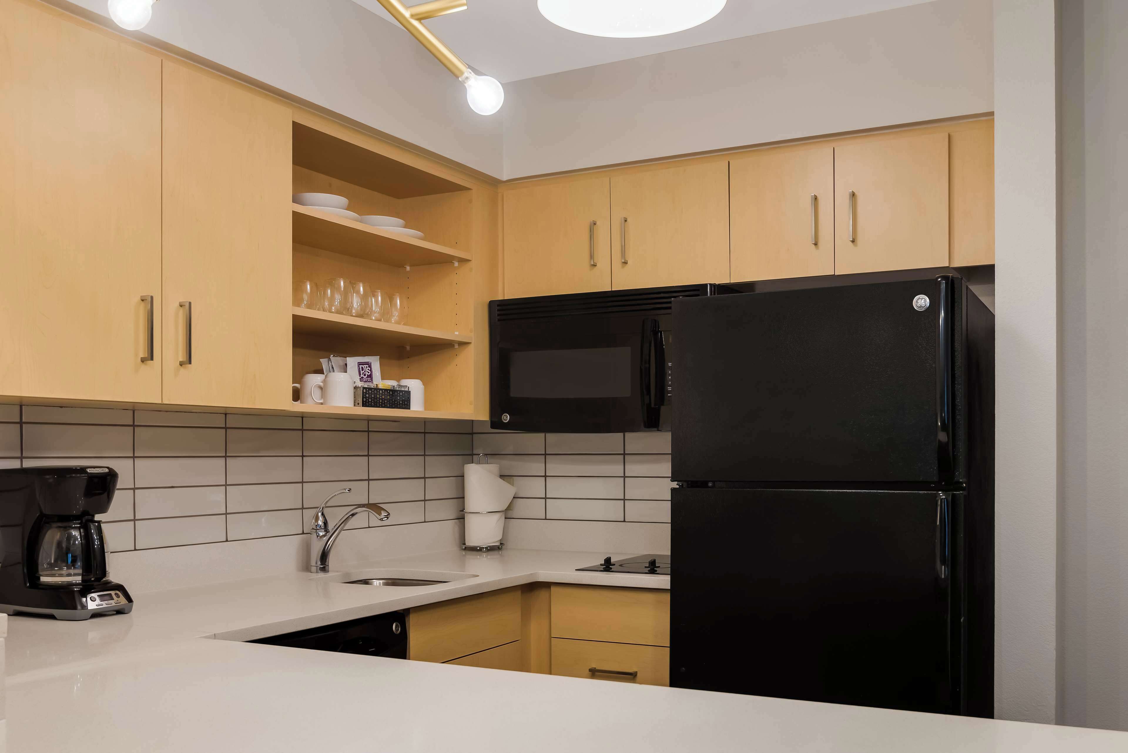 A modern kitchen with wooden cabinets, a black refrigerator, a coffee maker, and a microwave.