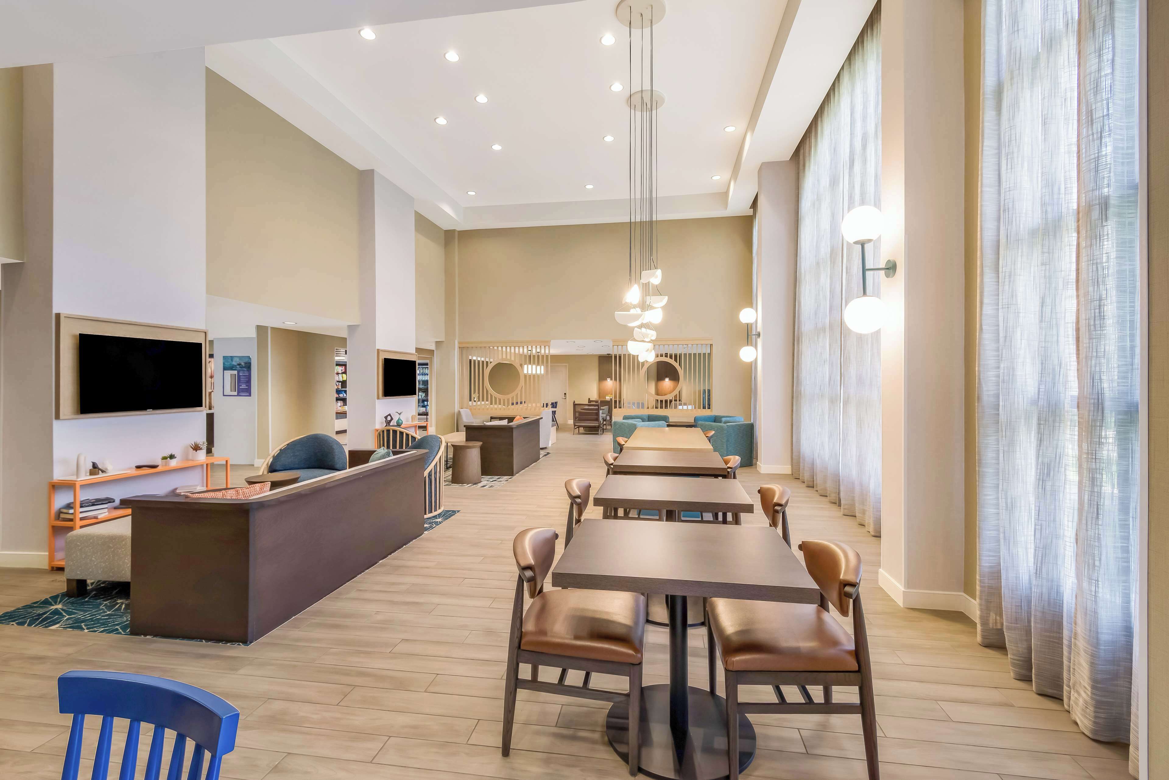 A spacious hotel lobby with a central seating area, a reception desk, and a television.
