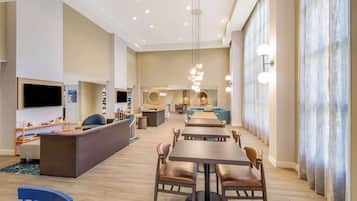 A spacious hotel lobby with a central seating area, a reception desk, and a television.