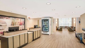 A hotel reception area with a reception desk, a beverage refrigerator, and a seating area with tables and chairs.