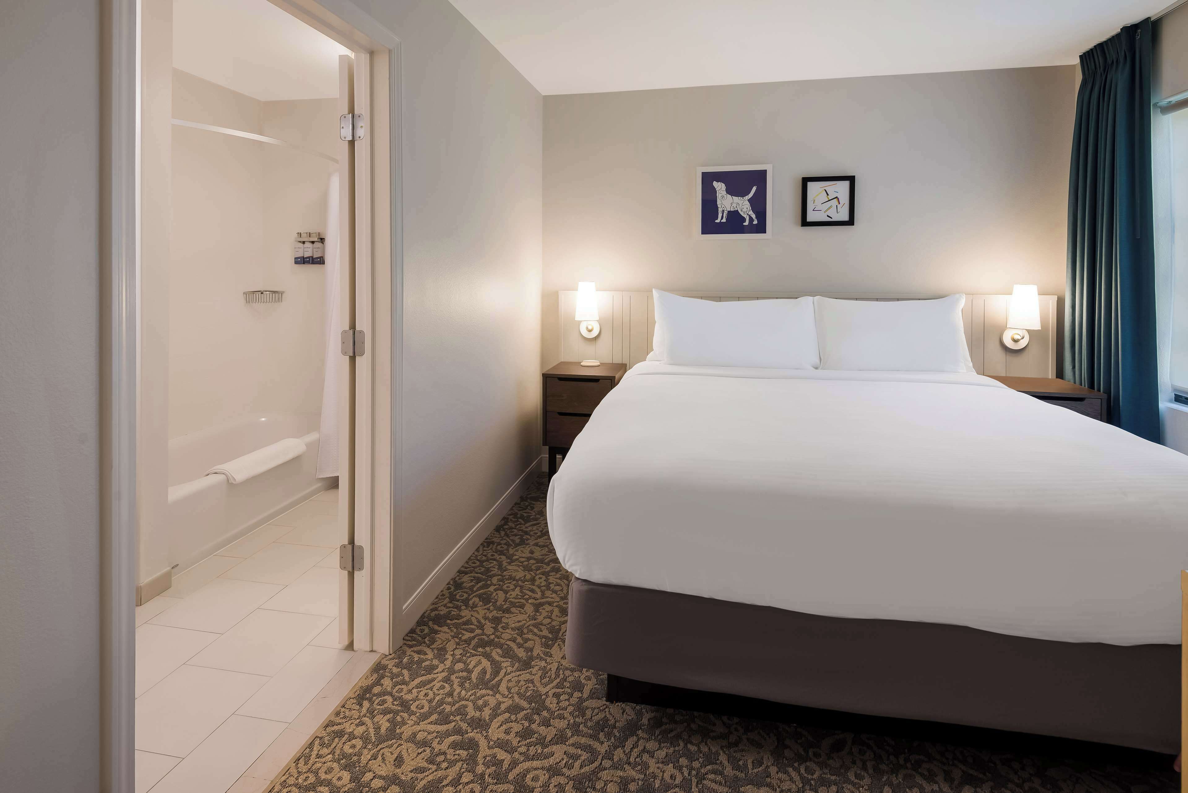 A hotel room with a large bed, two wall-mounted lamps, a shower, and a door leading to a bathroom.
