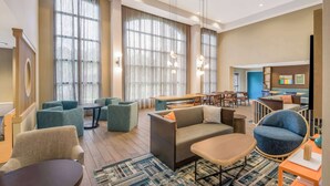 A modern hotel lobby with seating areas, a dining space, and large windows.