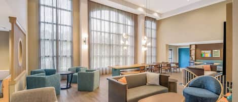 A modern hotel lobby with seating areas, a dining space, and large windows.