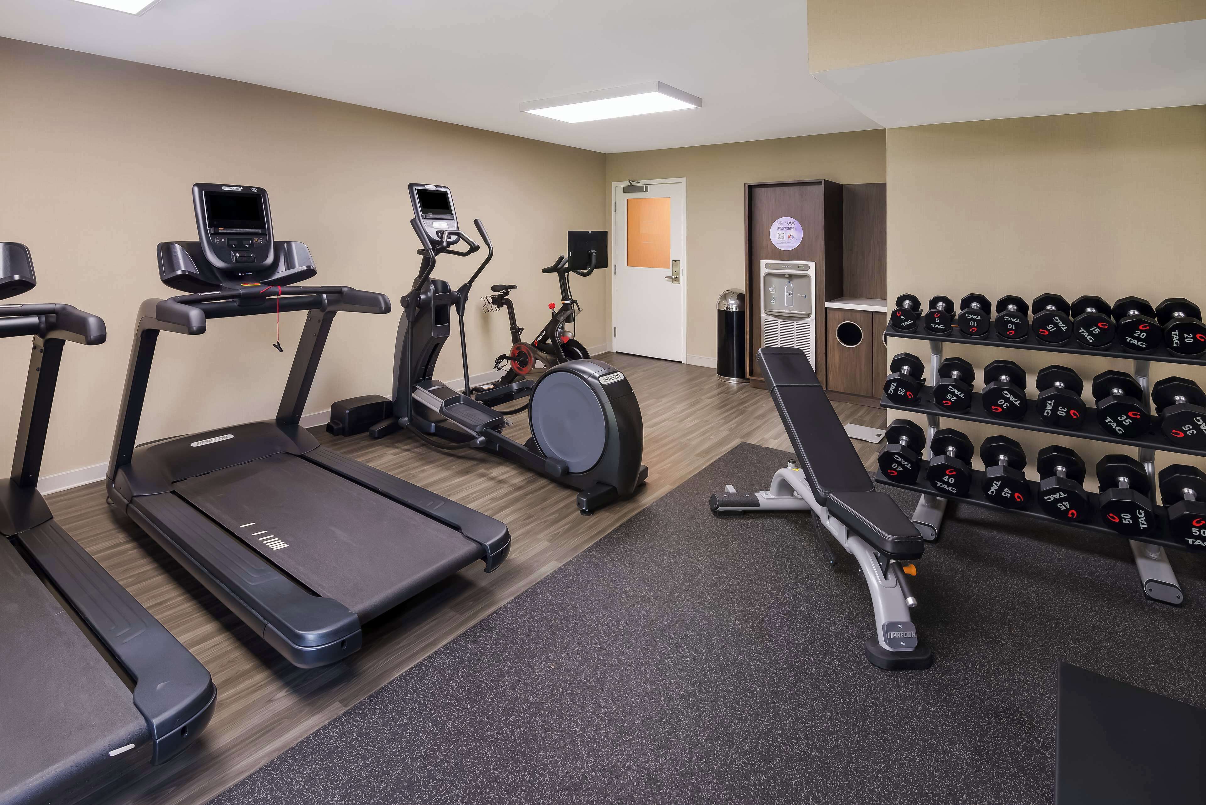 A gym with treadmills, an elliptical, a stationary bike, and a bench with dumbbells.