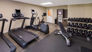 A gym with treadmills, an elliptical, a stationary bike, and a bench with dumbbells.