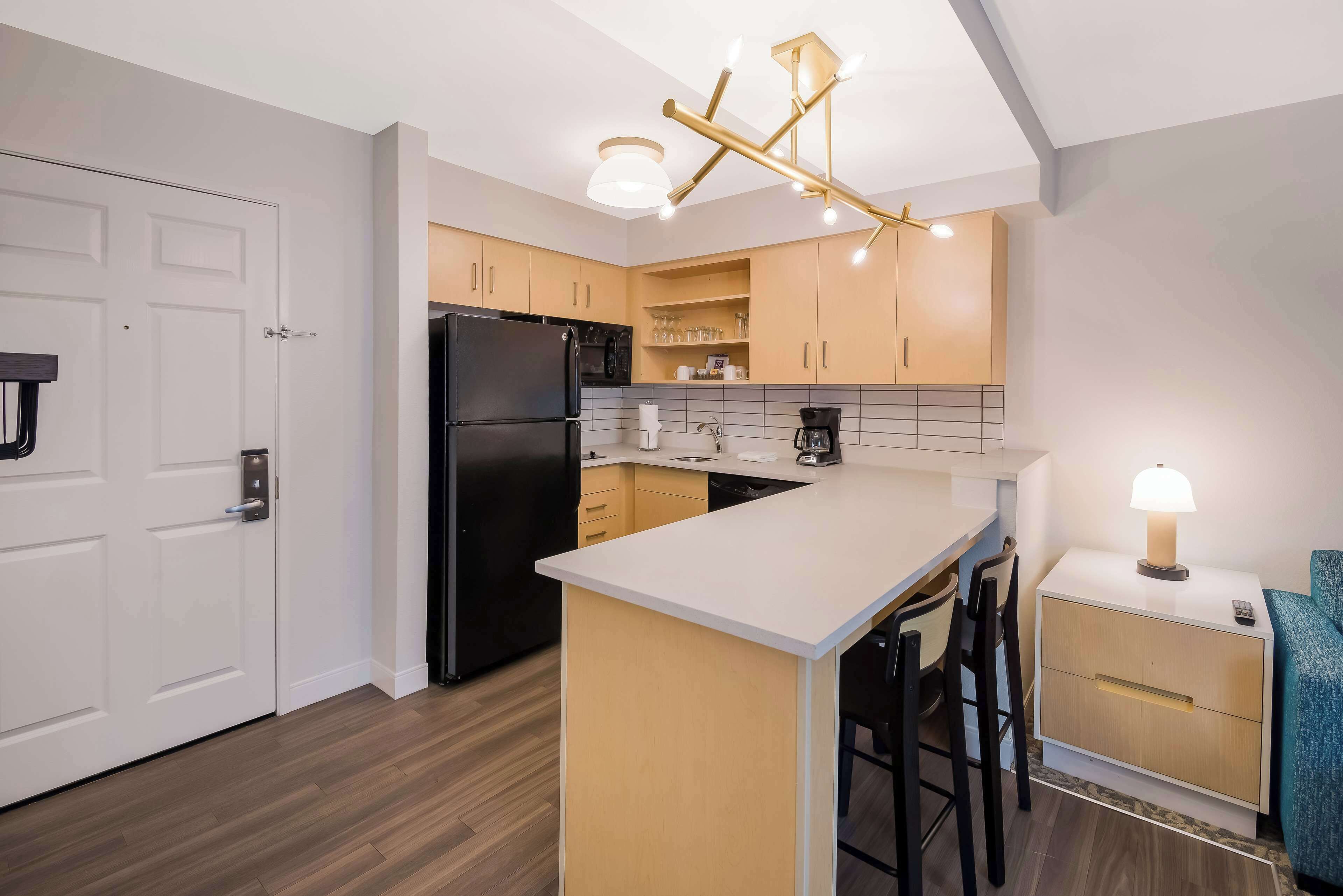 A modern kitchen with a central island, a black refrigerator, wooden cabinets, and a pendant light fixture.