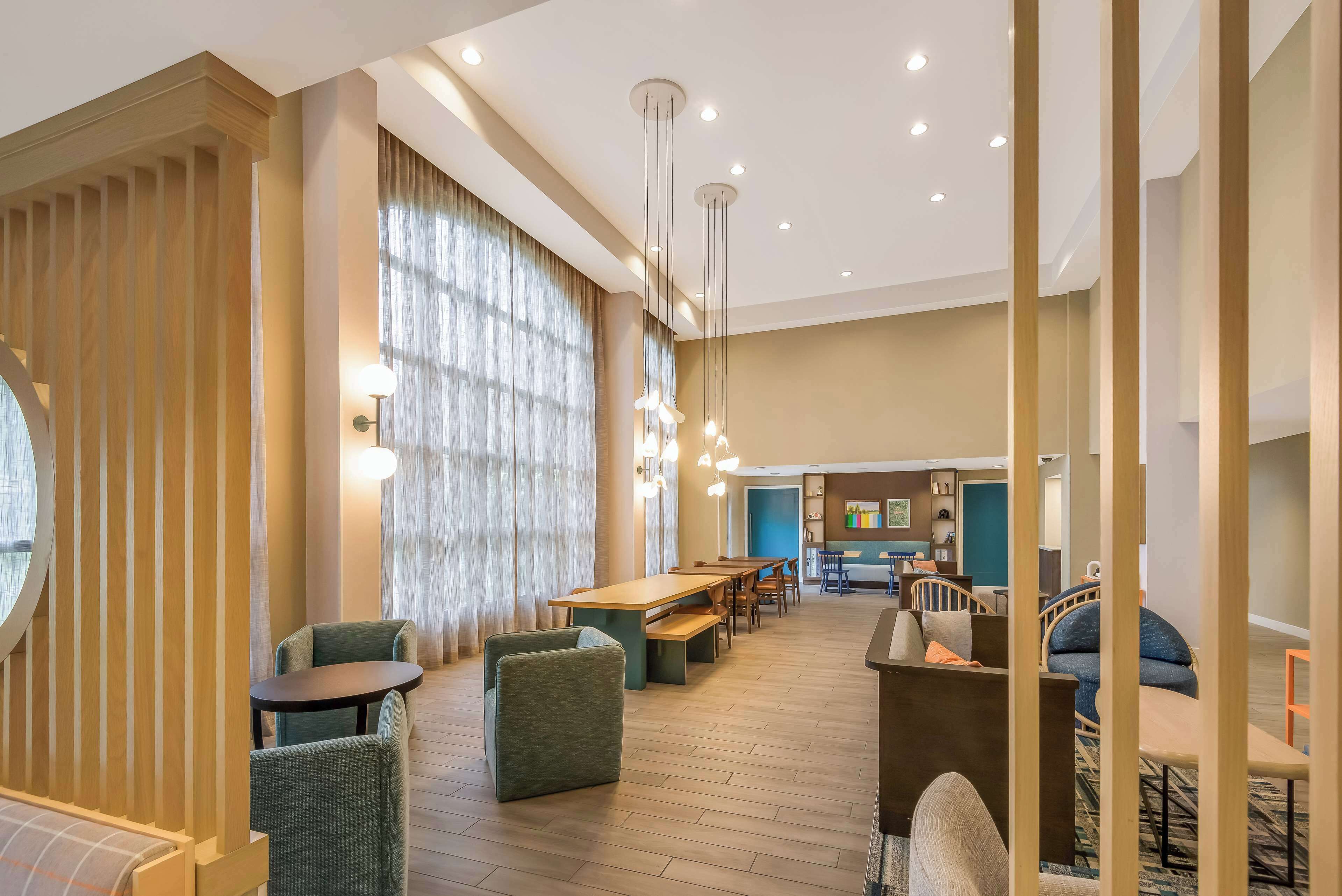 A modern hotel lobby with a wooden reception desk, seating area, and a dining space.