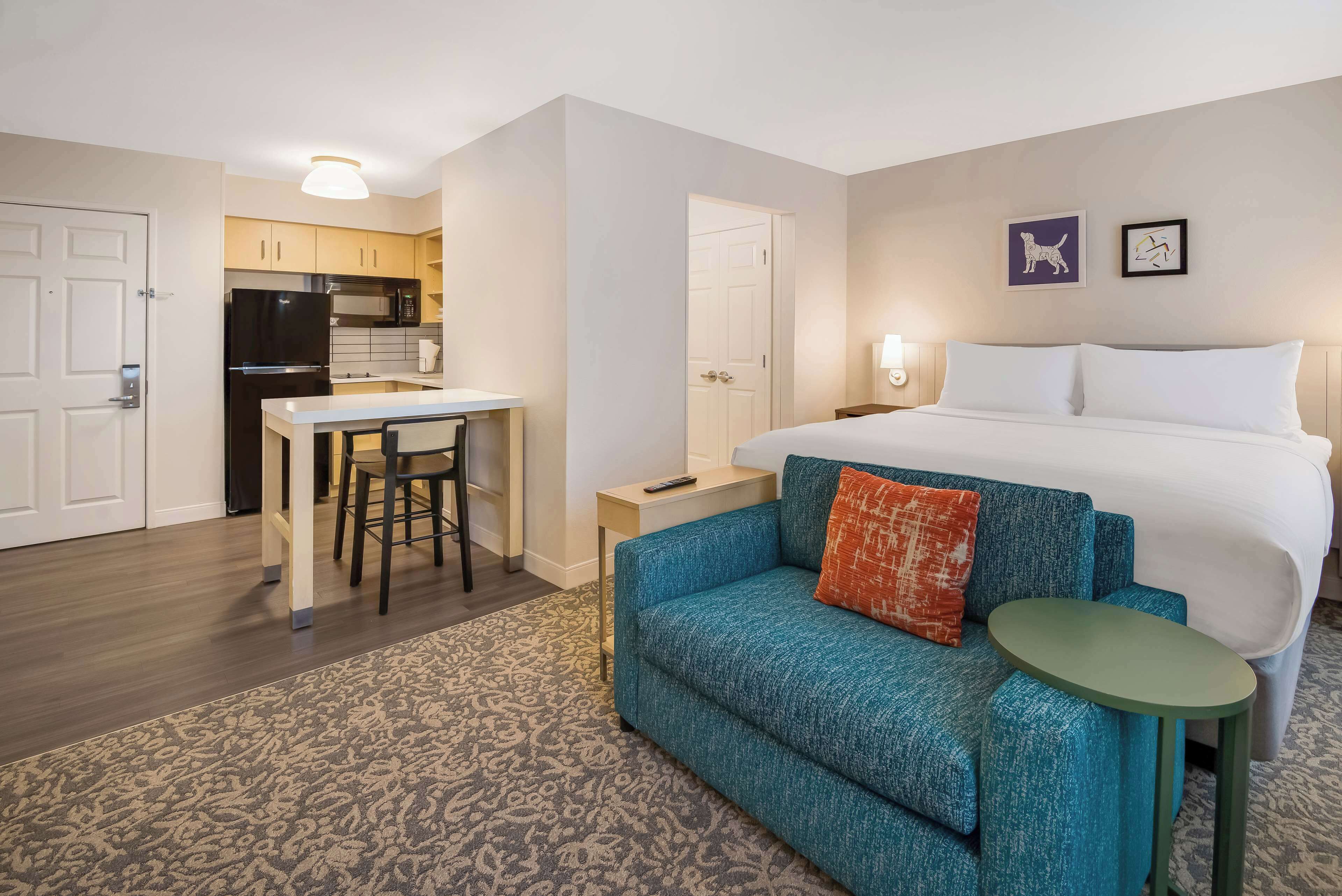 A hotel room with a bed, a sofa, a small table, a kitchen area, and a bathroom.