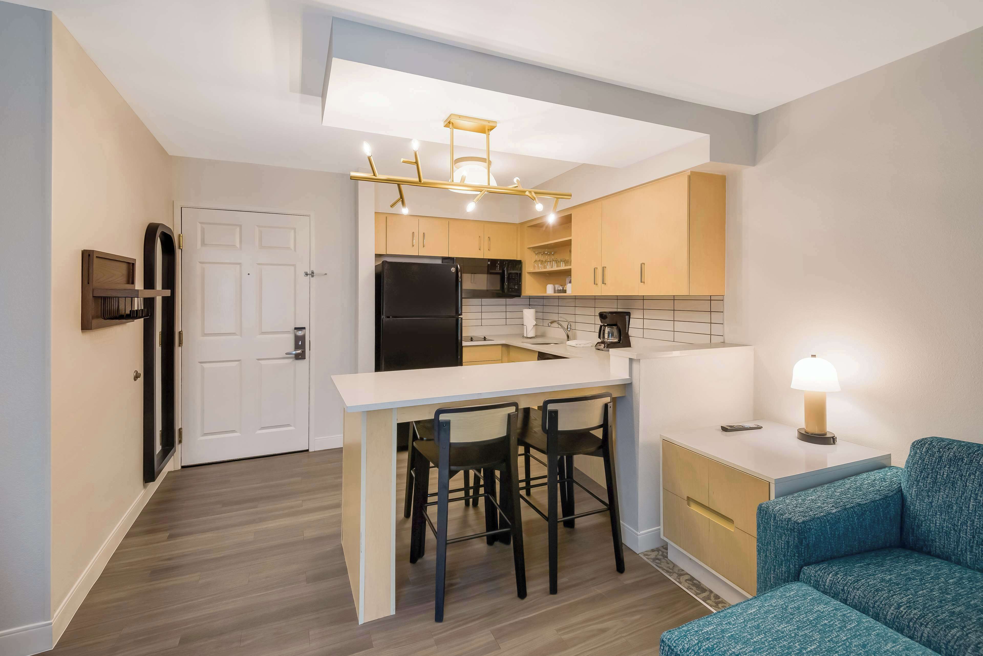A compact kitchen with a refrigerator, microwave, and coffee maker. There is a small dining area with a table and two chairs.