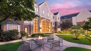 A residential building with a stone facade, large windows, and a landscaped front yard with a fire pit and outdoor seating.