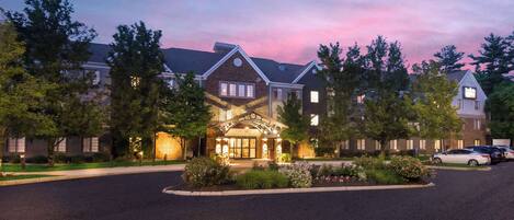 A hotel with a traditional architectural style, featuring a central entrance with a decorative archway, surrounded by well-maintained landscaping and parked cars.