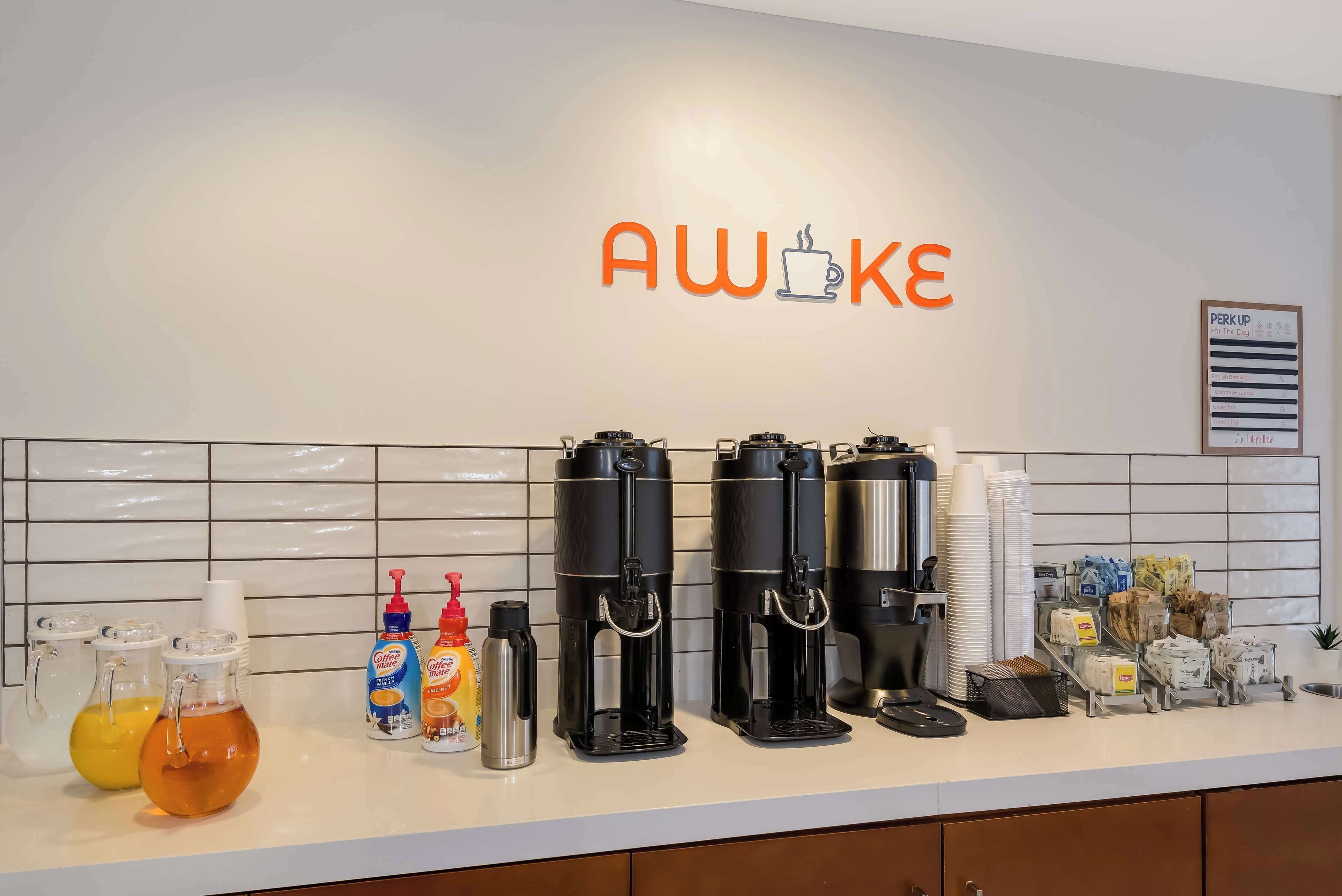 A coffee station with multiple coffee makers, condiment dispensers, and a branded sign.