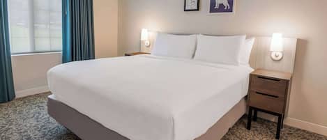 A hotel room with a large bed, two bedside tables, a window with curtains, and two wall-mounted lamps.