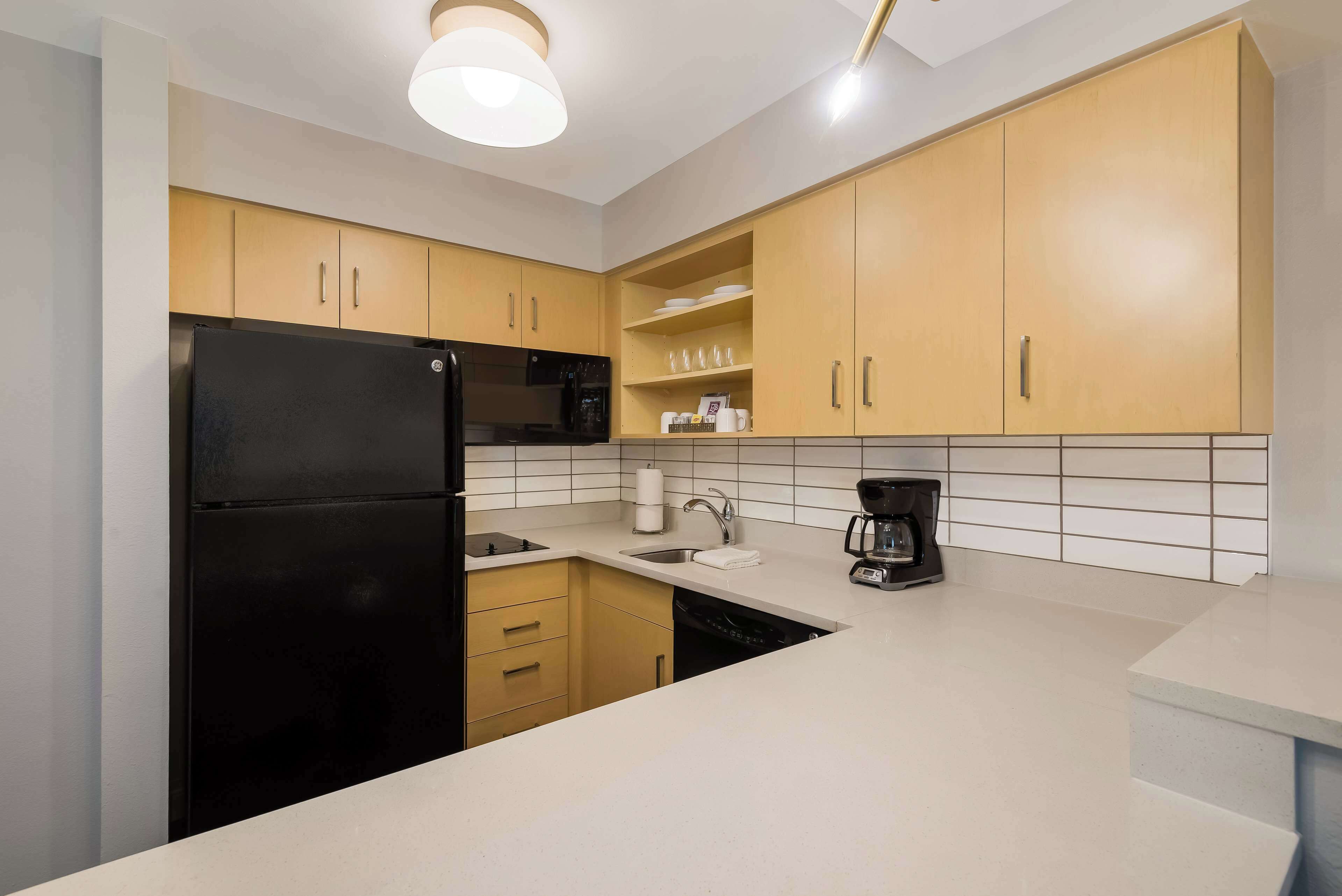 A modern kitchen with a black refrigerator, a coffee maker, and wooden cabinets.