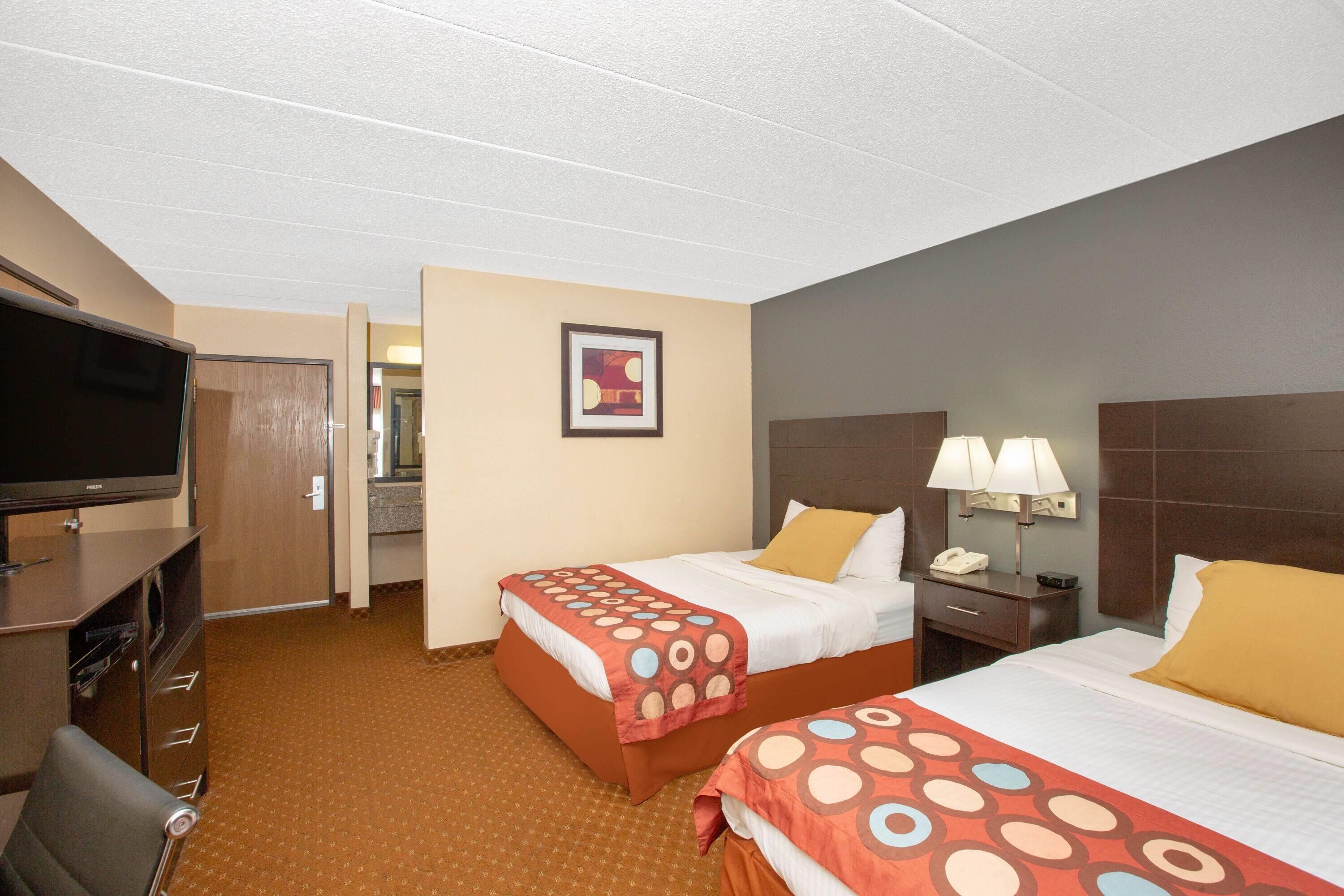 A hotel room with two beds, a television, a desk with a lamp, and a painting on the wall.