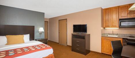 Una habitación de hotel con cama, escritorio, televisor, microondas y kitchenette.