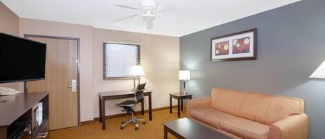 Habitación de hotel con televisión, escritorio, silla de oficina, sofá y ventilador de techo.