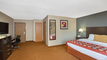Una habitación de hotel con una cama, un escritorio con televisor, una silla, una lámpara de escritorio y una mesita de noche.