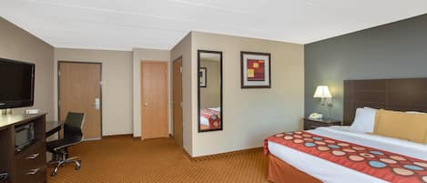 A hotel room with a bed, a desk with a television, a chair, a desk lamp, and a nightstand.