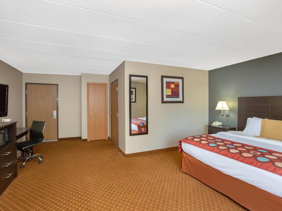 Una habitación de hotel con una cama, un escritorio con televisor, una silla, una lámpara de escritorio y una mesita de noche.