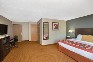 A hotel room with a bed, a desk with a television, a chair, a desk lamp, and a nightstand. - Baymont by Wyndham Coralville (Coralville)